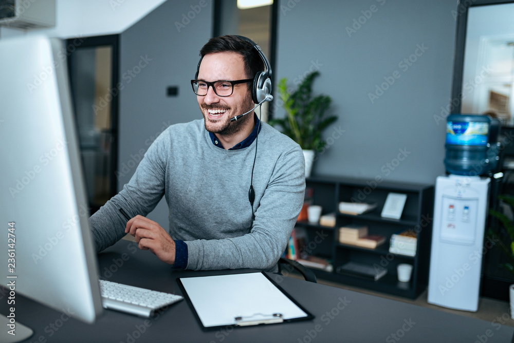 一个戴着耳机在电脑上工作的英俊微笑男子的肖像。