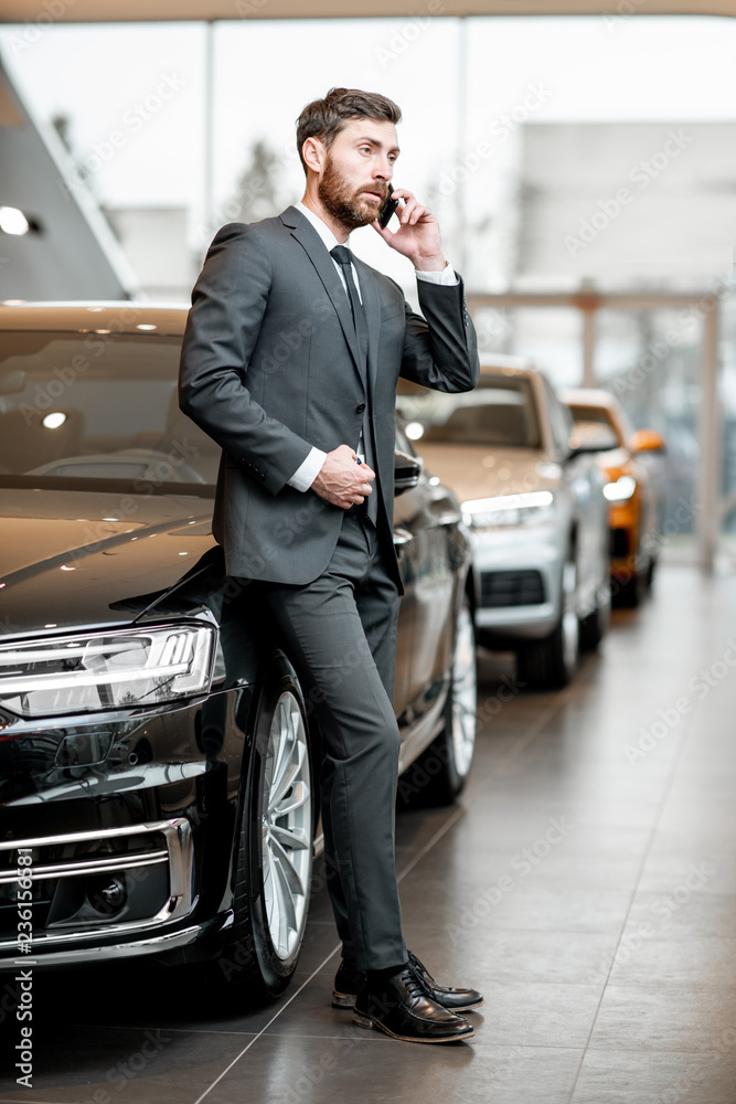 穿着西装的优雅商人或销售人员在汽车展厅里打电话
