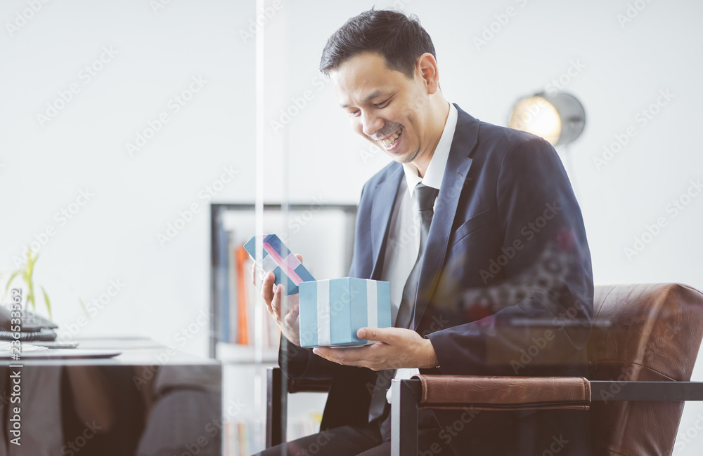 Asian Businessman happy smile open christmas gift box from client in office .