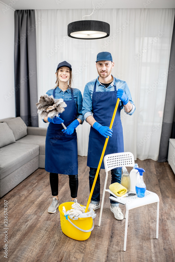 Portrait of a young couple as a professional cleaners in blue uniform with cleaning tools in the apa