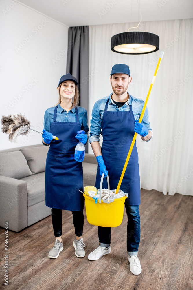 Portrait of a young couple as a professional cleaners in blue uniform with cleaning tools in the apa