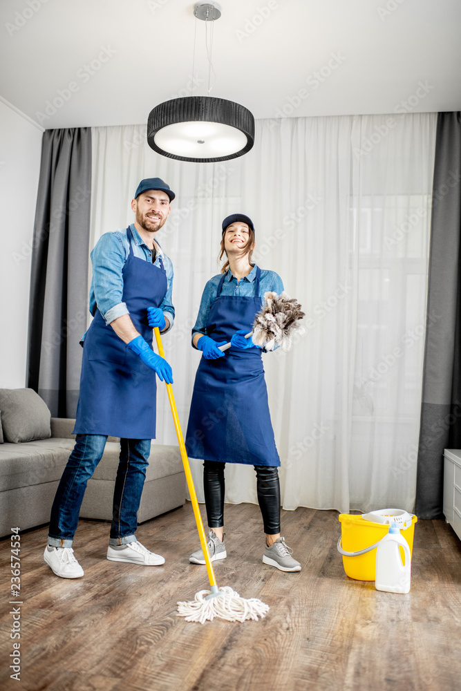 一对年轻夫妇的画像，他们是一名身穿蓝色制服、在公寓里拿着清洁工具的专业清洁工