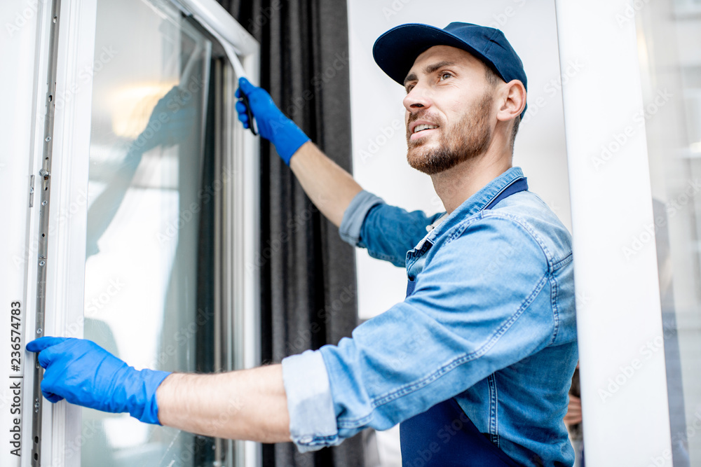 男子作为专业清洁人员穿着蓝色制服在室内用橡胶刷清洗窗户