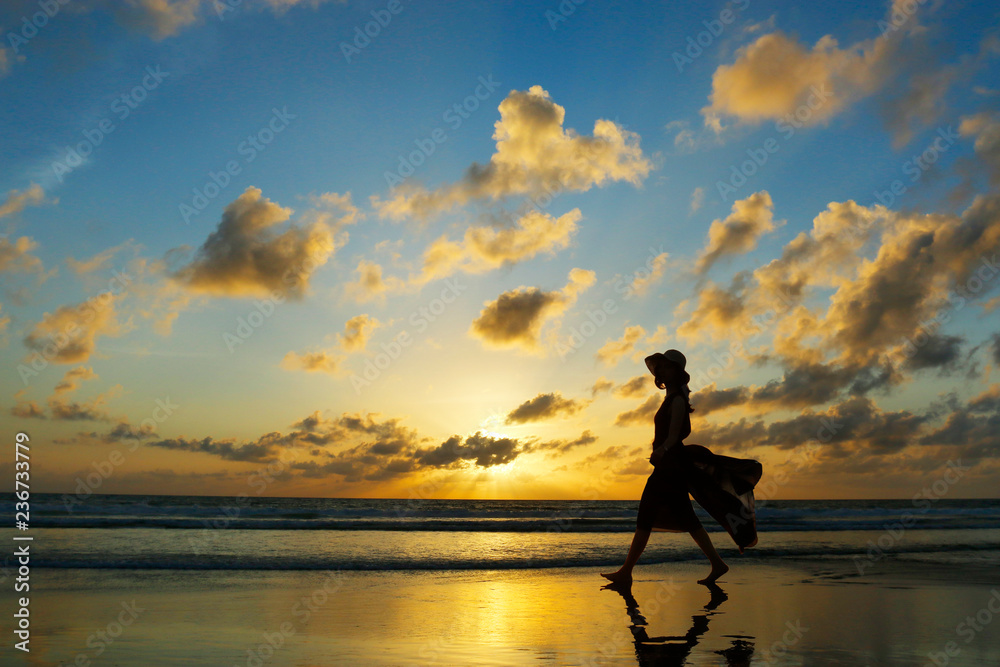 日落时走在海滩上的女人的剪影