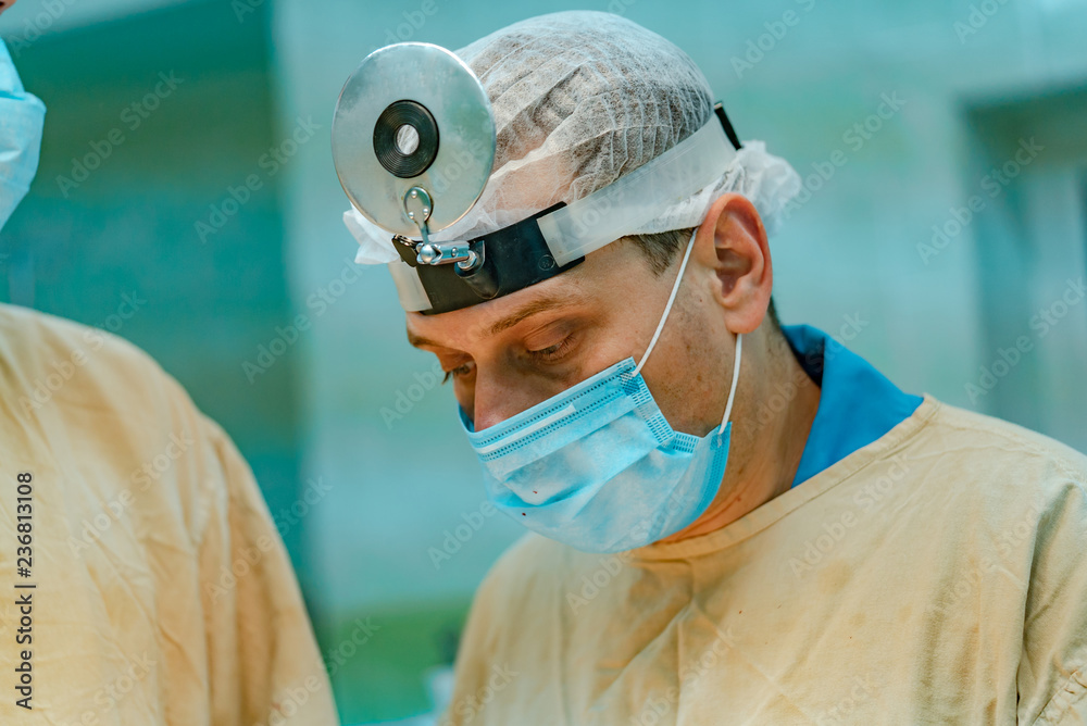 手术室里，一名身穿医用服、头上戴着放大镜的外科医生。外科医生