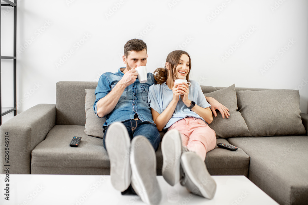 一对穿着休闲的年轻夫妇一起坐在沙发上，在家看电视