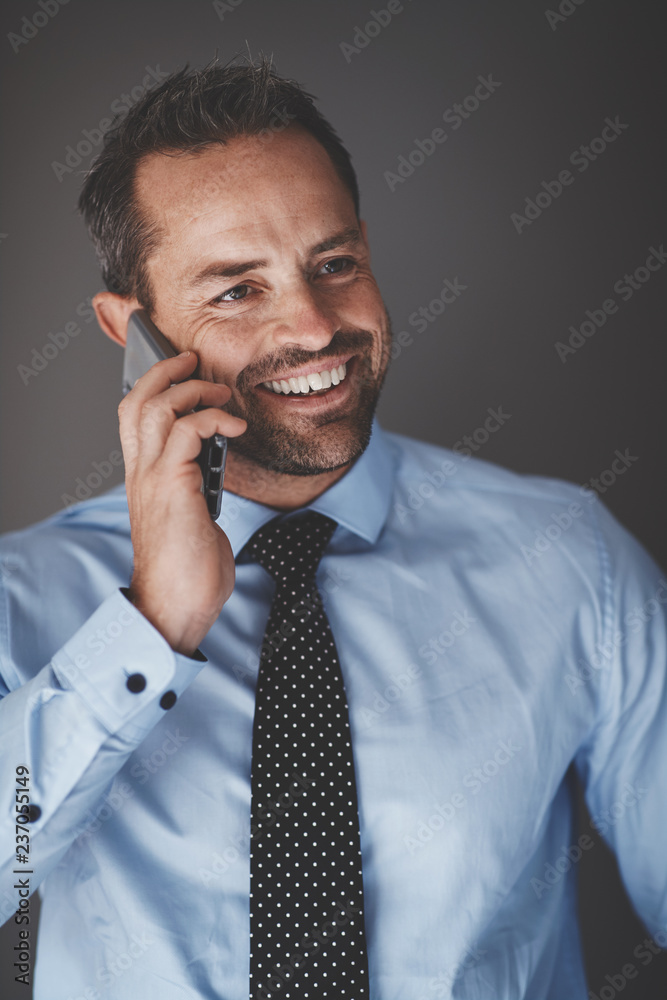 微笑的商人靠着灰色的背在手机上说话