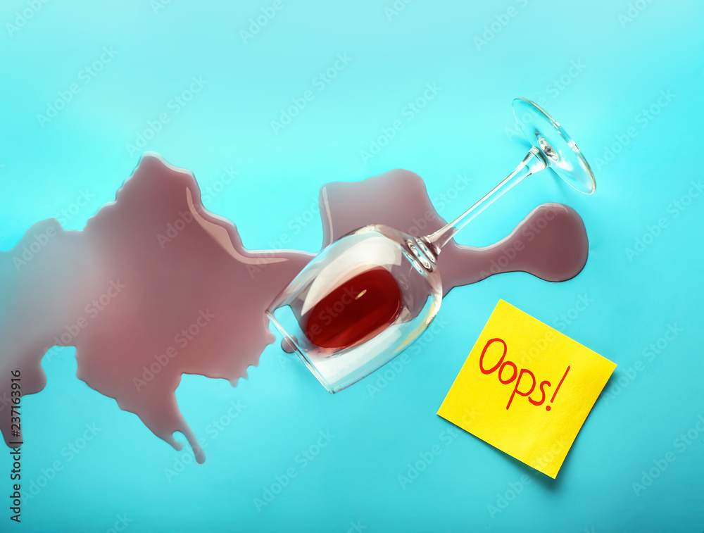 葡萄酒从翻倒的玻璃和纸卡片上溢出，背景颜色为OOPS。概念错误