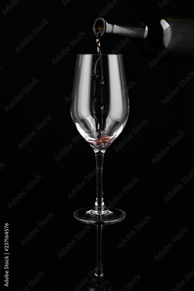 在深色背景下将红酒从瓶中倒入玻璃杯