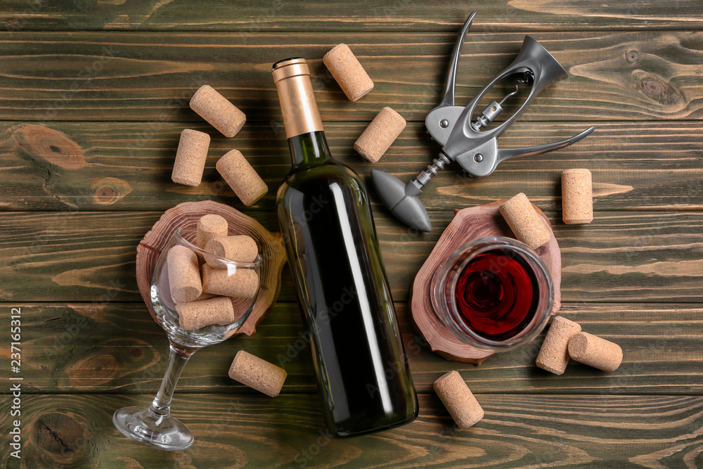 Bottle and glass of red wine with corkscrew on wooden background