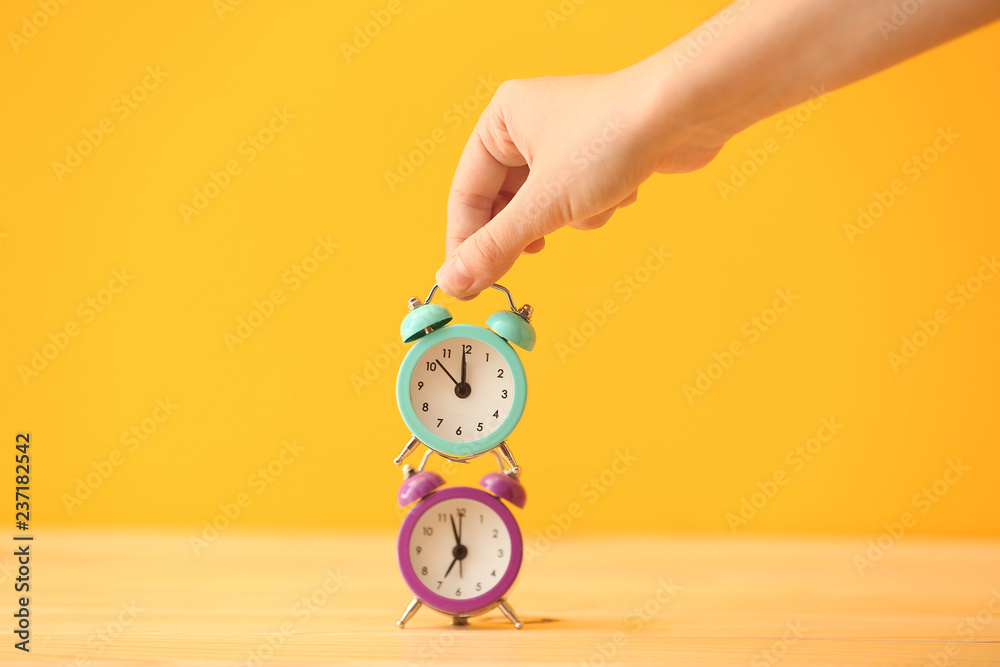 Woman stacking alarm clocks on color background