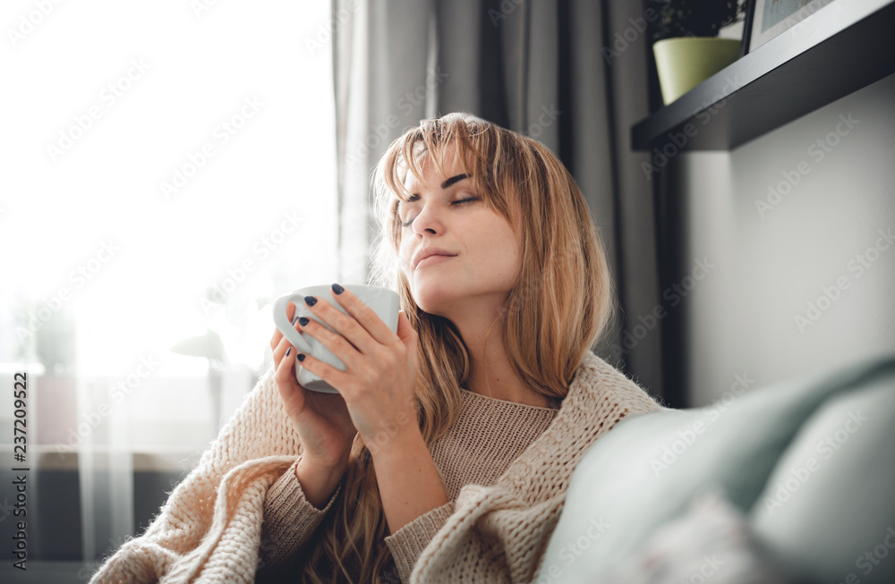 穿着柔软毛衣的快乐女人在家里喝杯热茶或咖啡放松