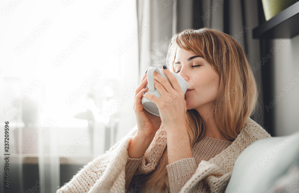 穿着柔软毛衣的快乐女人在家里喝杯热茶或咖啡放松