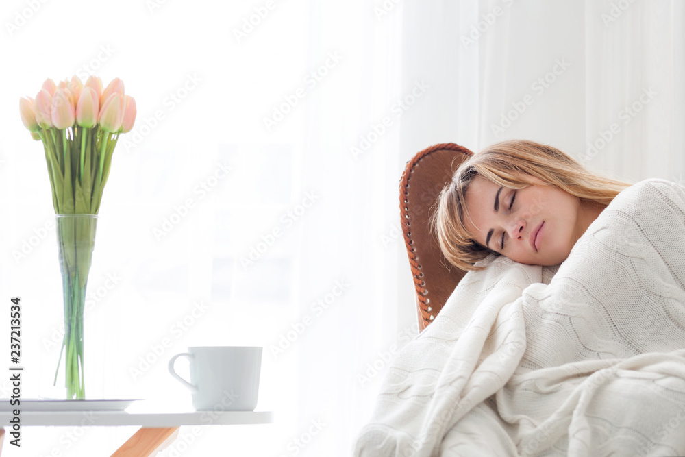 熟睡的年轻女子拥抱柔软的针织毯子，在舒适的家里坐在扶手椅上放松