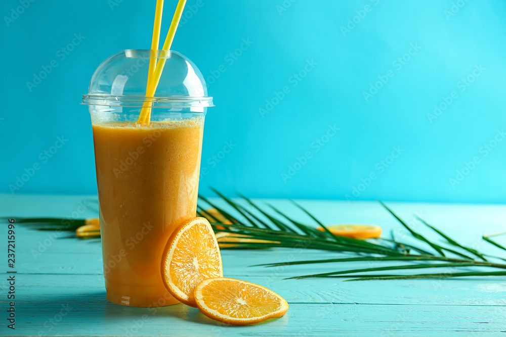 彩色木桌上的美味橙色奶昔塑料杯