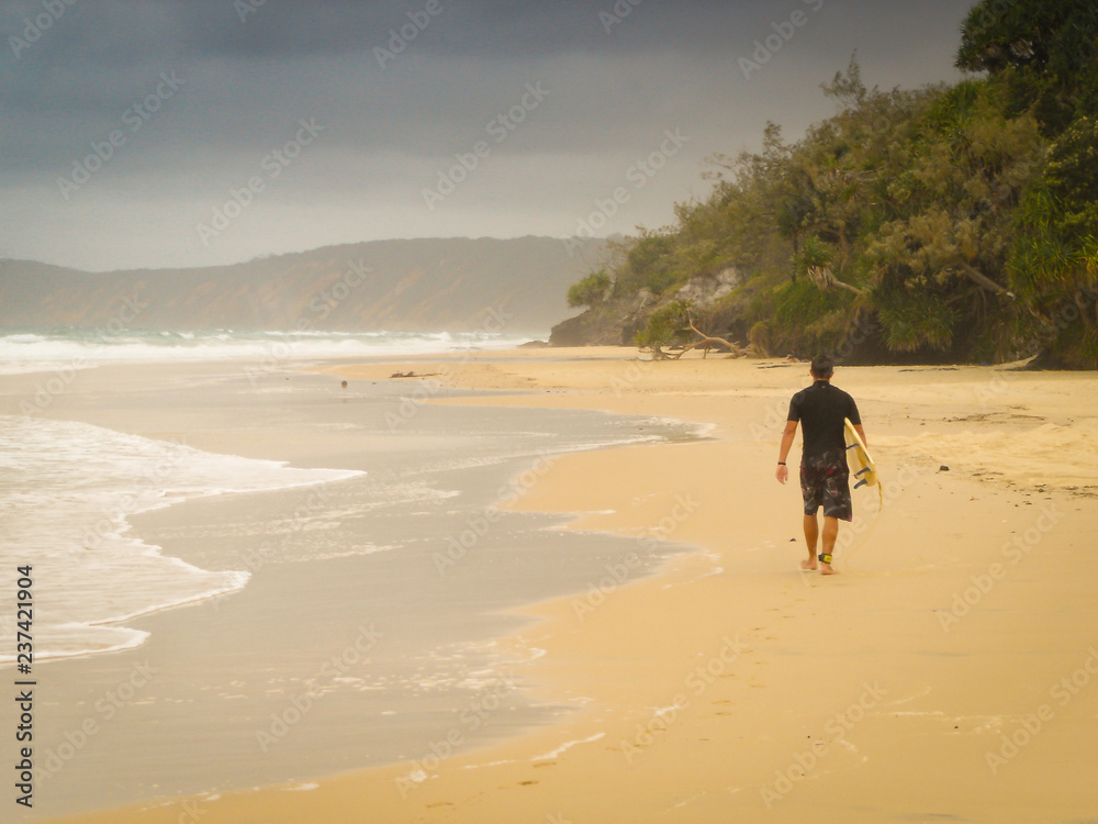 一名冲浪者独自带着冲浪板在海滩上的水边行走