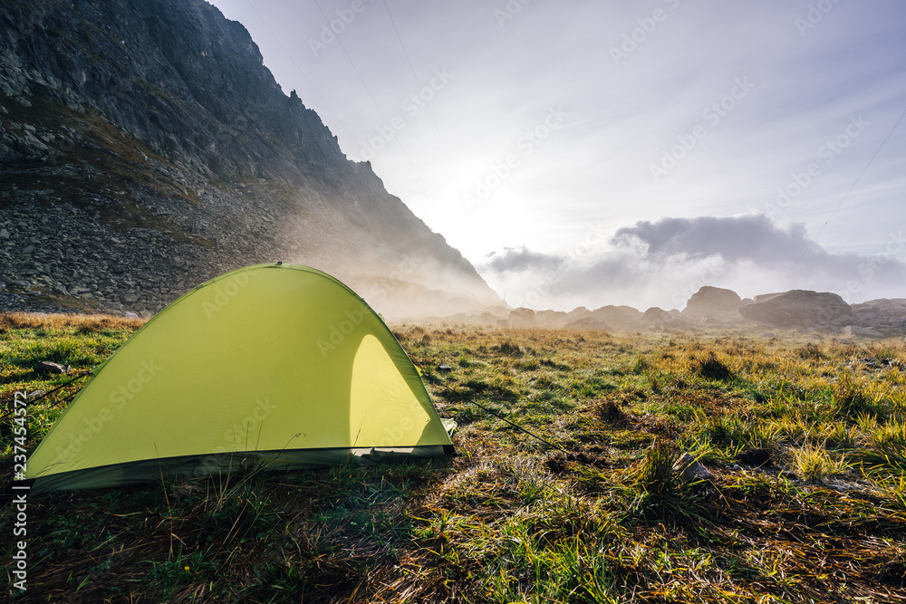 一个绿色的帐篷搭在高山般的绿草中。清晨日出薄雾弥漫