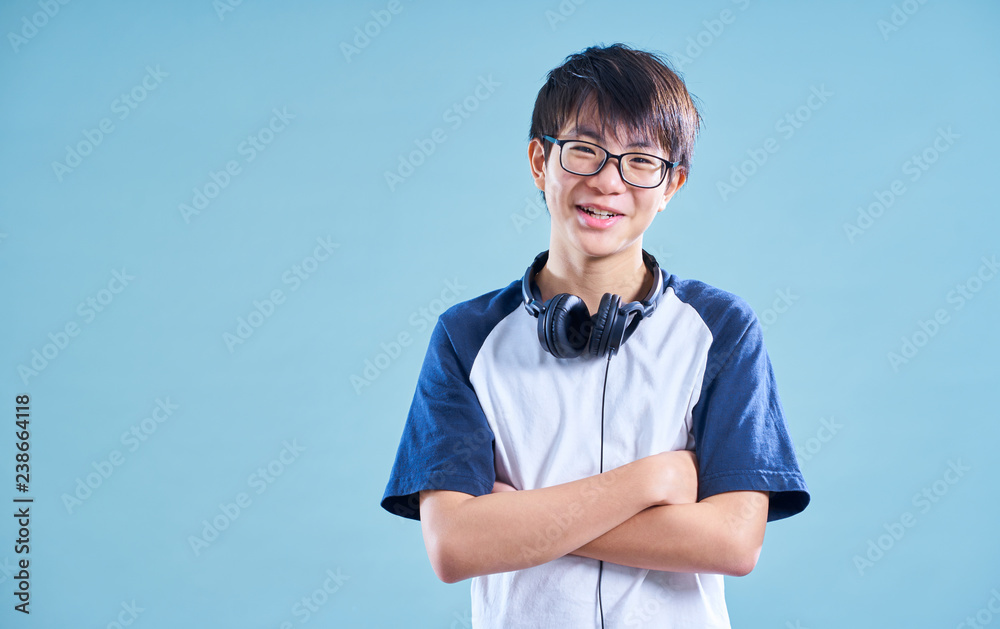 浅蓝色背景的亚洲十几岁微笑男孩的肖像。音乐耳机概念