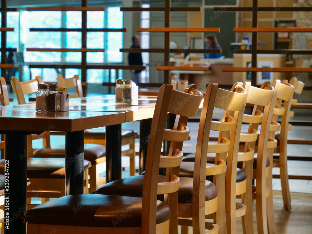 特写：机场餐厅的桌子周围摆放着空的木椅。