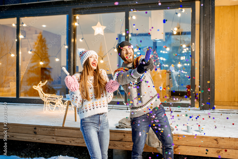 一对年轻幸福的夫妇穿着毛衣，在装饰精美的房子前庆祝寒假