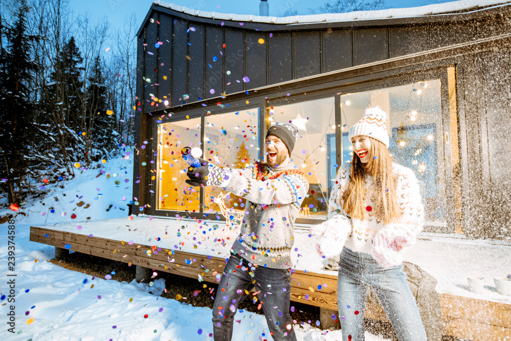 一对年轻幸福的夫妇穿着毛衣在装饰精美的房子前庆祝寒假