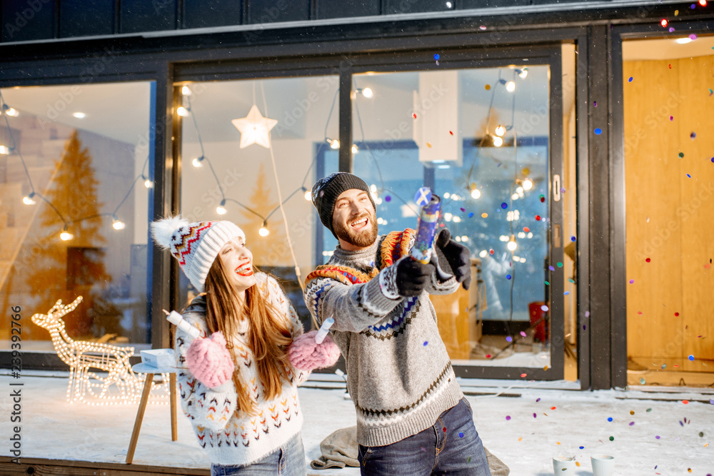 年轻幸福的一对情侣穿着毛衣在装饰精美的房子前庆祝寒假