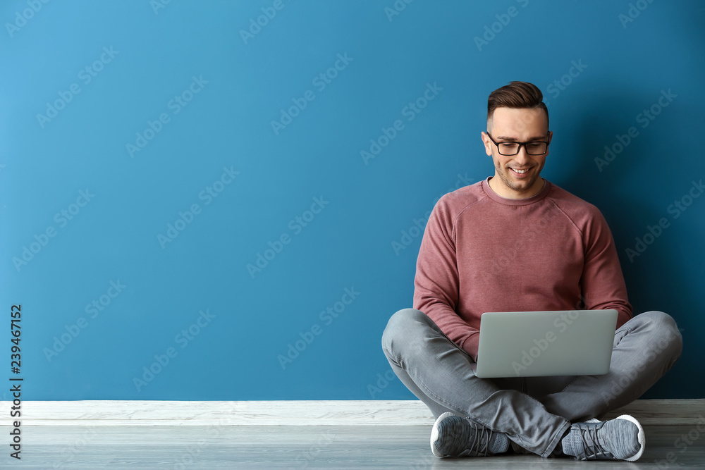 年轻人拿着笔记本电脑坐在彩色墙上