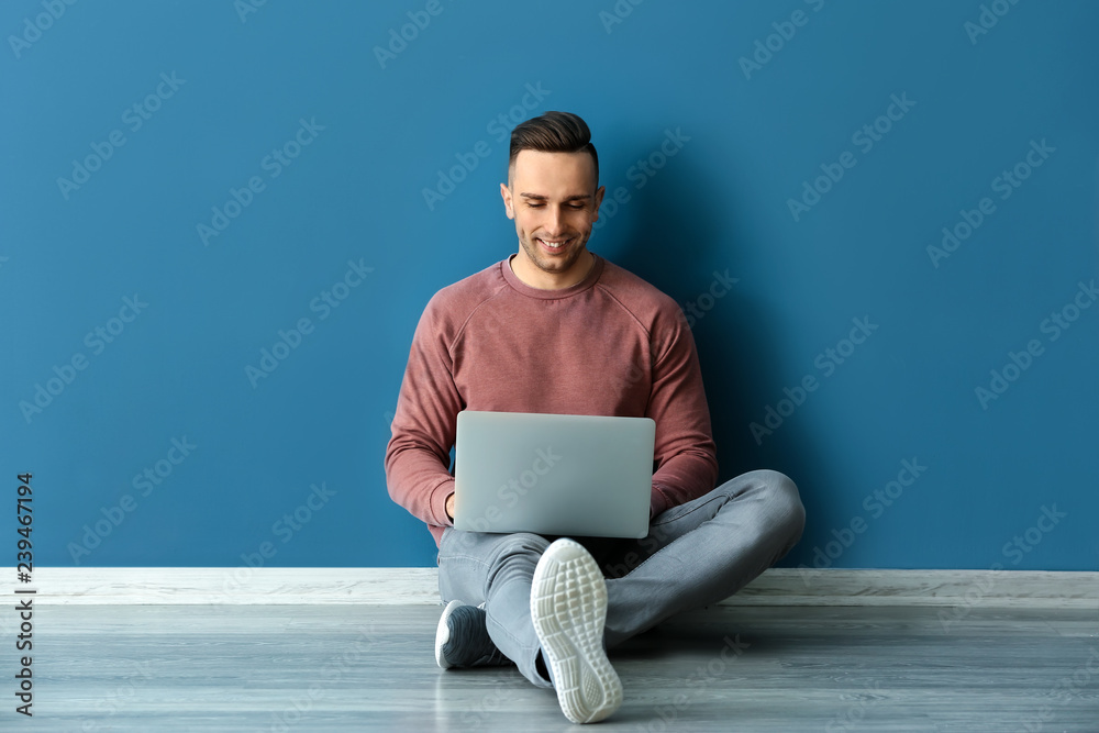 年轻人拿着笔记本电脑坐在彩色墙上