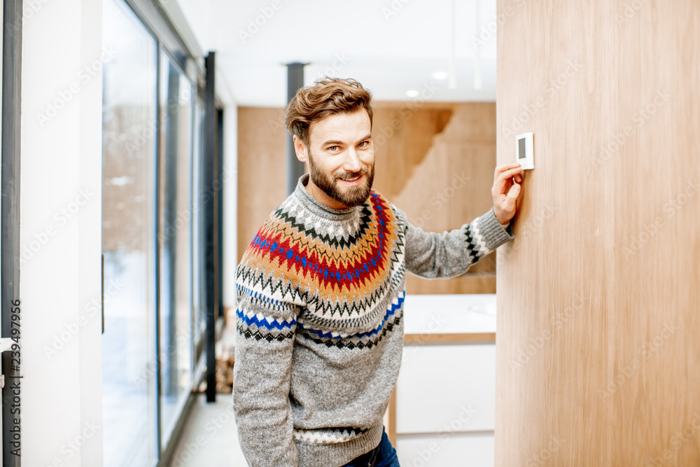 穿着毛衣的男人在家里用电子恒温器调节室温