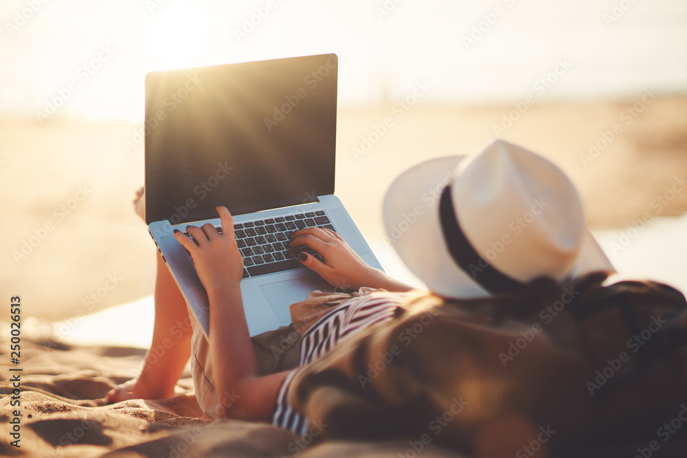 年轻女子在海滩上用笔记本电脑在大自然中工作。