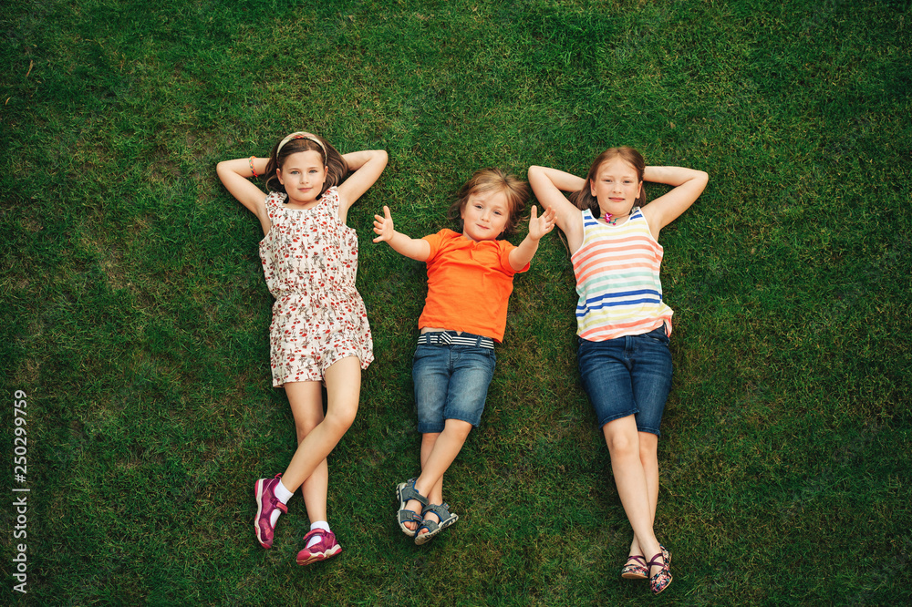 快乐的孩子们在户外玩得很开心。孩子们在夏季公园玩耍。小男孩和两个女孩躺在地上