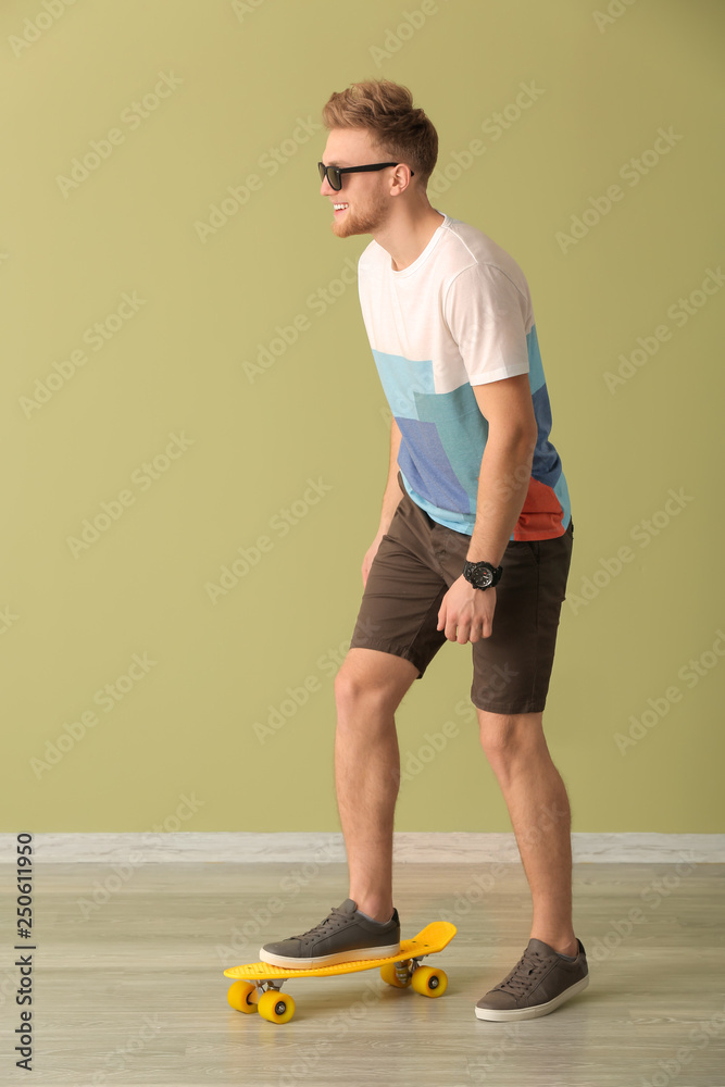 时尚年轻人在彩色墙附近玩滑板