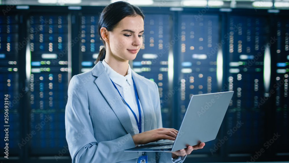 女性IT专家正在数据中心服务器机架旁边的笔记本电脑上工作。