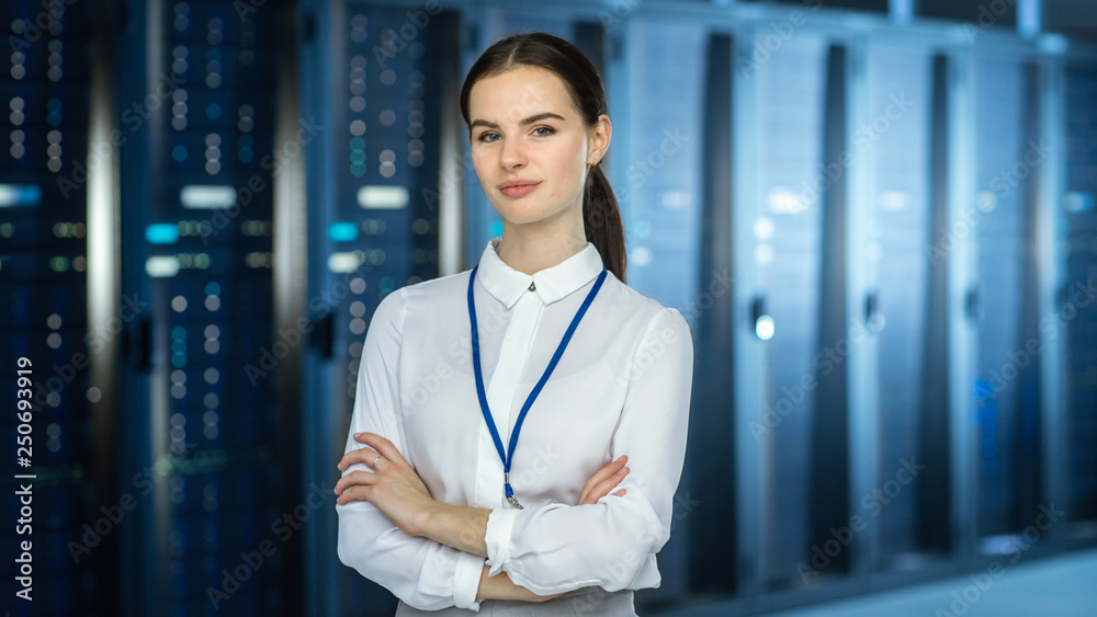 Female IT Specialist is standing at the Camera in Data Center Next to Server Racks and Looking at th