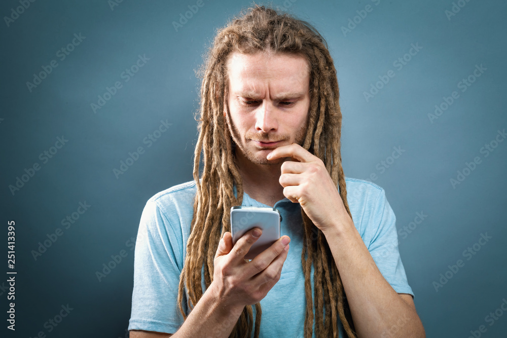 Young man staring at his cellphone on a gray background