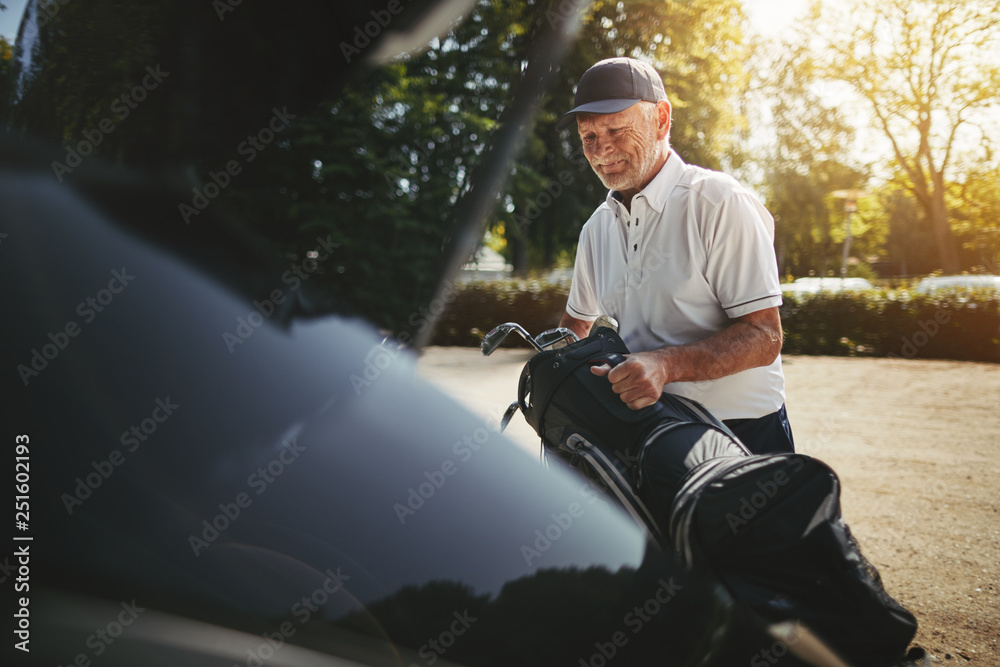 一位老人把他的高尔夫球杆装在汽车后备箱里