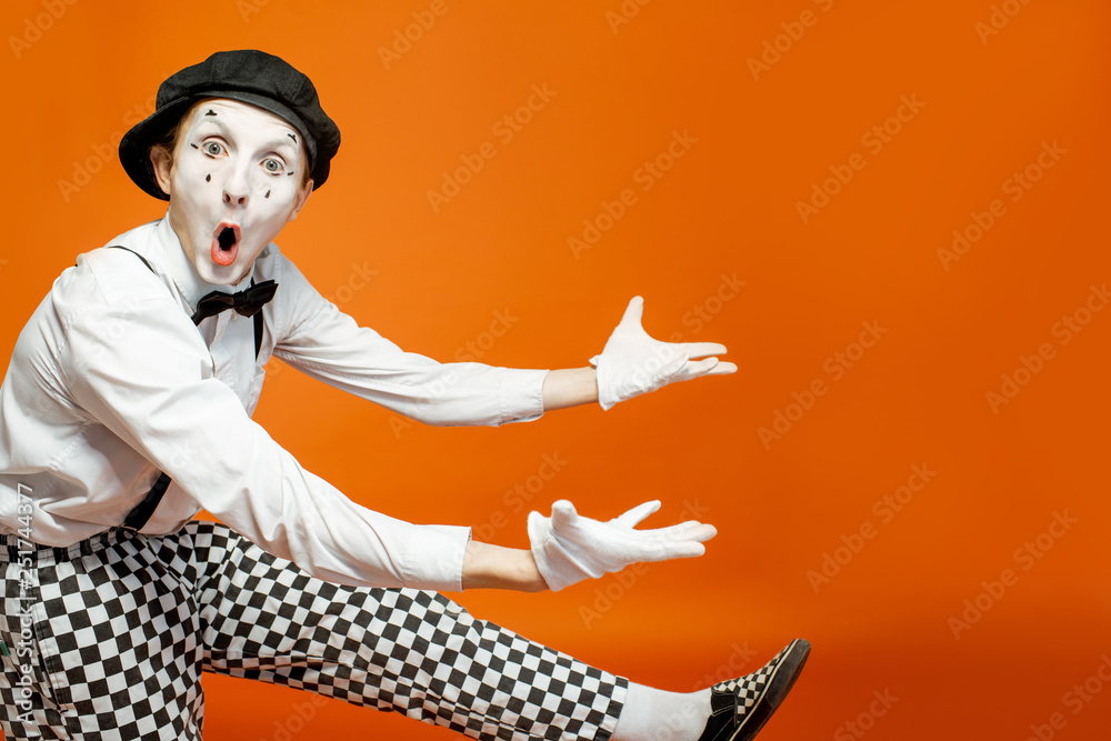 Emotional pantomime with white facial makeup showing empty space on the orange background, advertisi