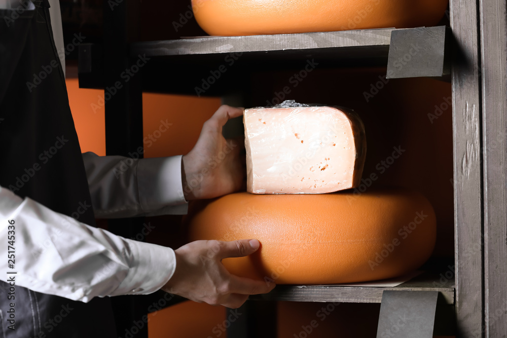 Male seller near rack with delicious cheese in store