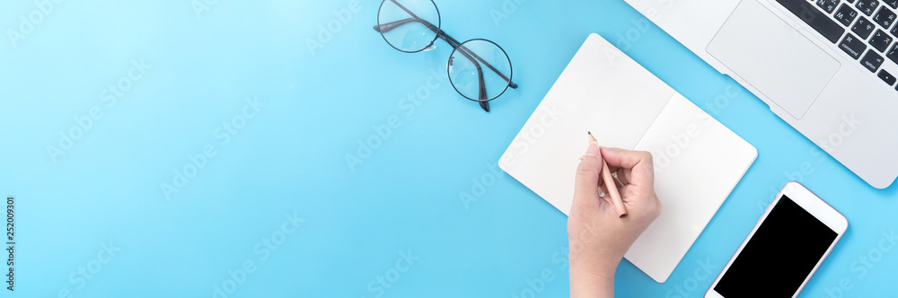 一名学生在家里一个最小的干净的蓝色工作场所，在打开的白皮书或会计上写作