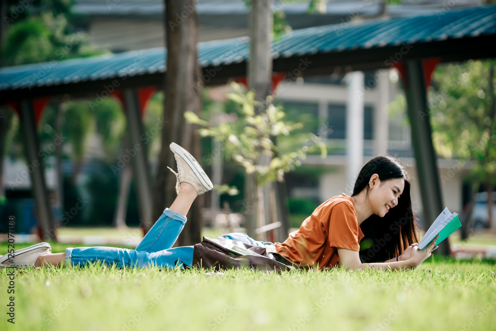 一个年轻或十几岁的亚洲女学生在大学里微笑着看书，看着平板电脑