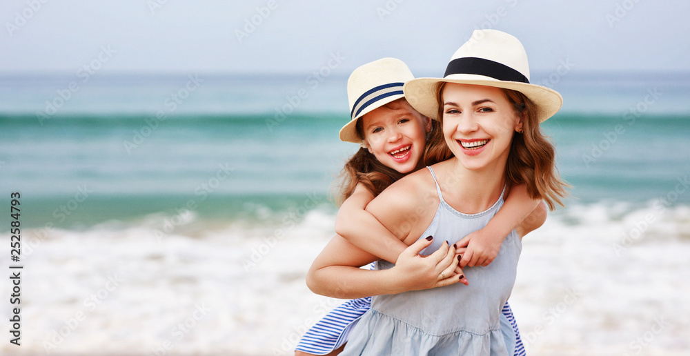 海滩上的幸福家庭。日落时母亲和孩子的女儿拥抱。