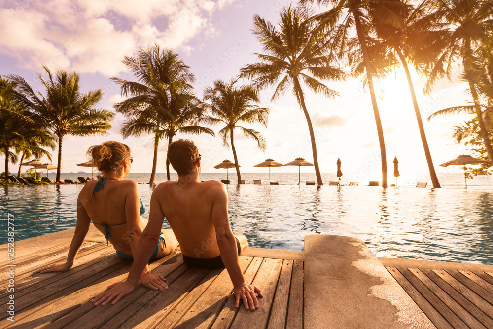 情侣在热带度假胜地享受海滩度假假期，这里有游泳池和椰子树