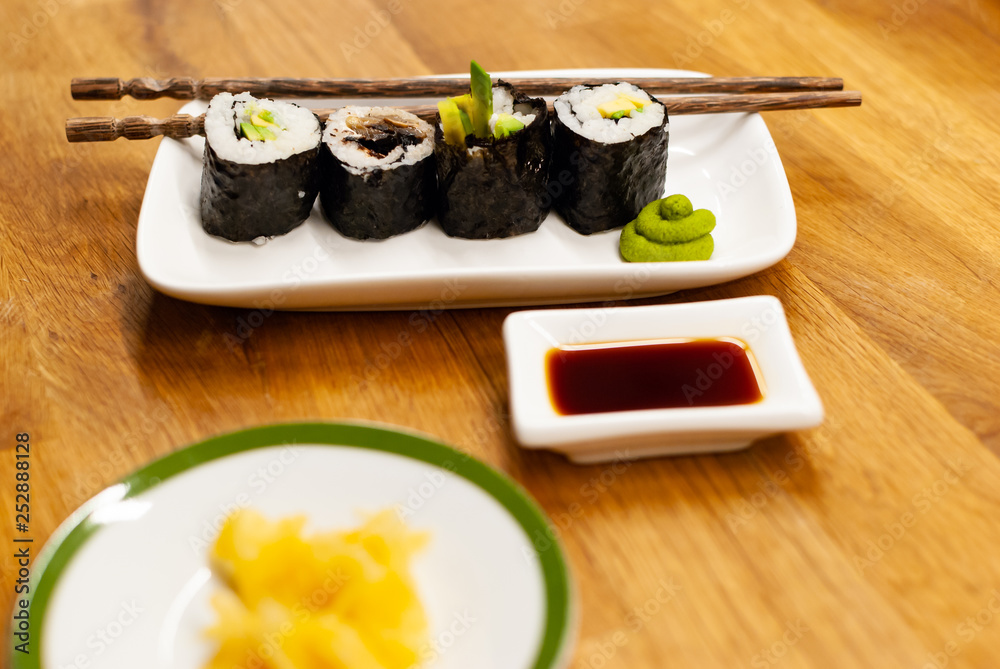 自制纯素食寿司卷，里面装着鳄梨，放在木桌上的一个小盘子里，里面放着酱油，哇