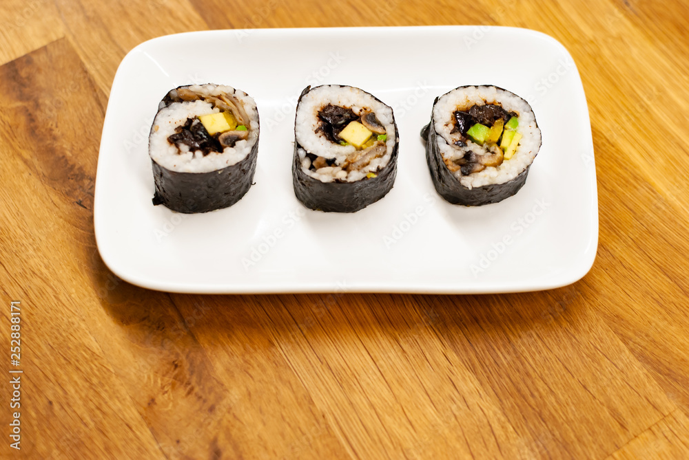 Homemade vegan Sushi rolls filled with avocado on a small plate on a wooden table with soy sauce, wa