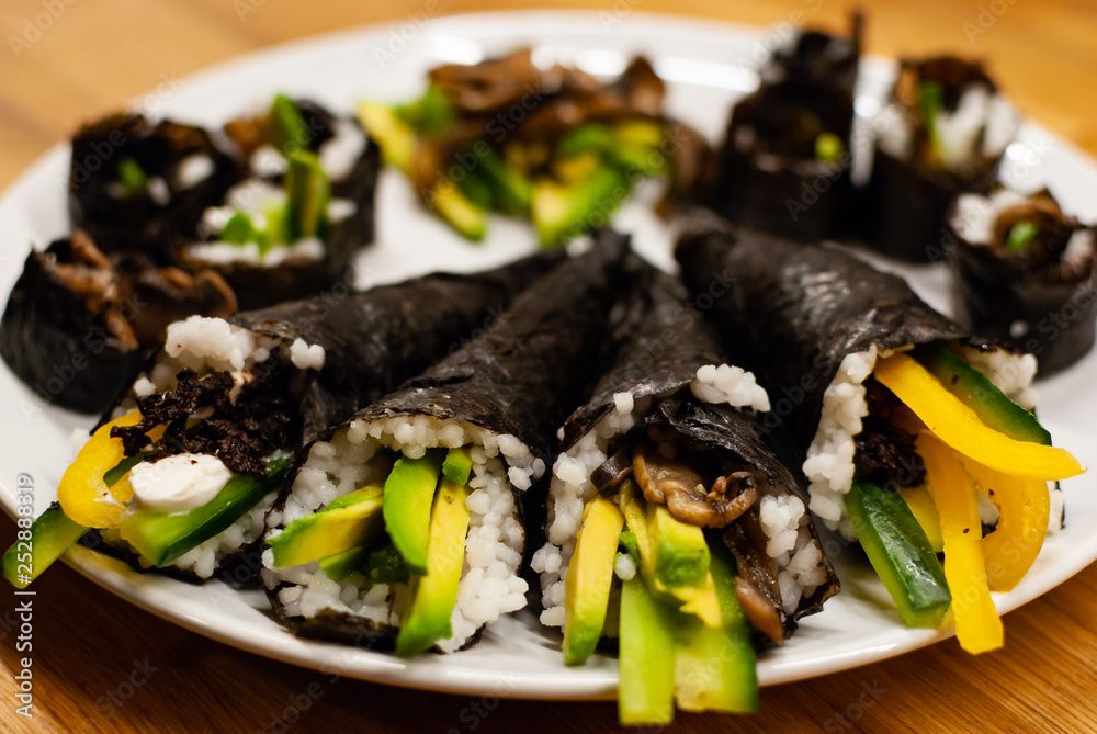 Homemade vegan Temaki-Sushi filled with avocado on a small plate on a wooden table with soy sauce an