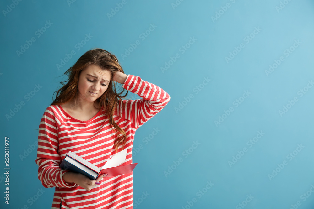 Emotional schoolgirl with books on color background