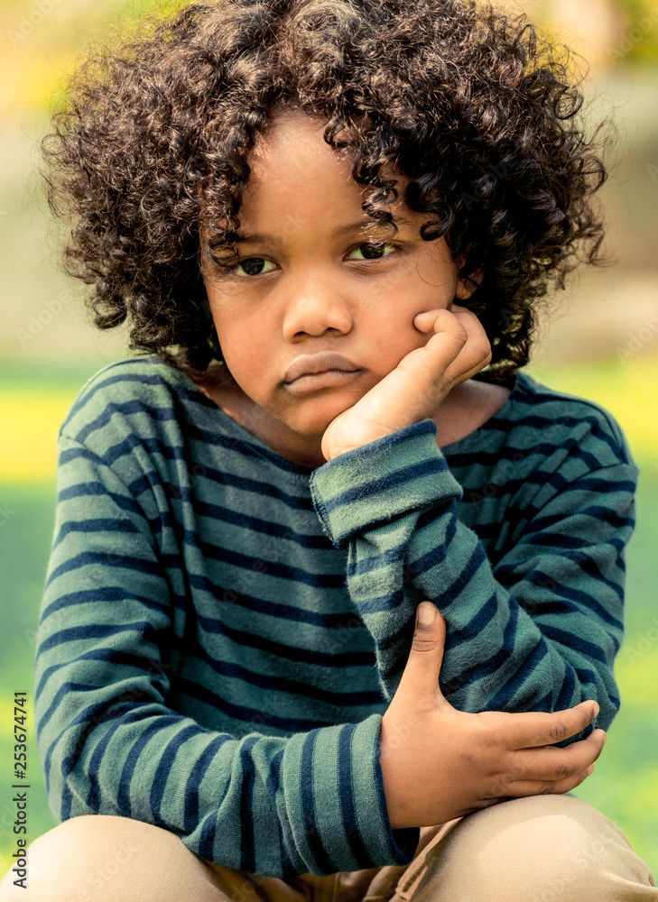 坐在公园里的一个不开心、无聊的非洲裔美国小孩。这个男孩表现出负面情绪。Chi