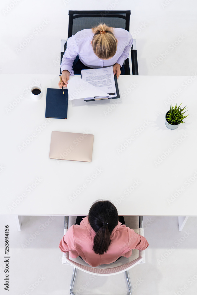 两位年轻的商业女性在办公桌上会面，申请工作和达成商业协议。Recr