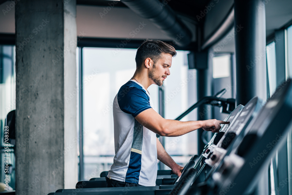 运动员在跑步机上调整速度，在健身房进行有氧运动的侧视图。