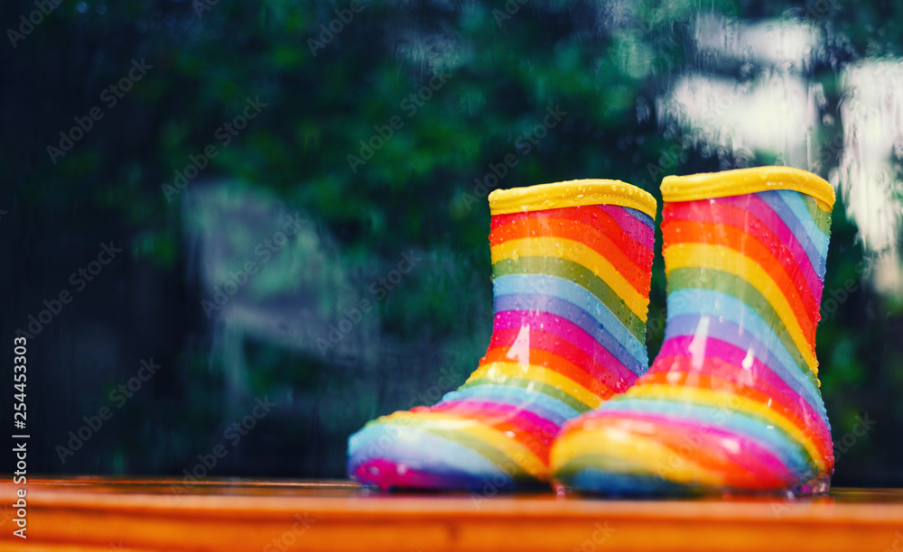 一双彩虹雨靴坐在外面，背景被雨水模糊了